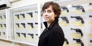 Lady with short brown hair stands in front of cabinet of weapons