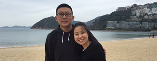 Dark haired man and woman stood on beach smiling