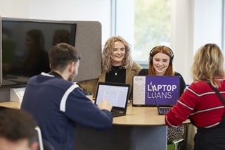 A group of students smiling and working on laptops