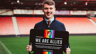 Male student in a sports stadium holds sign with slogan "We are allies"