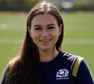 A female student standing in a playing field with goalposts in the background
