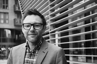 Black and white image of a man wearing a blazer, shirt and glasses
