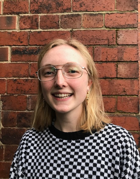 Young white woman with strawberry blonde hair, wearing glasses and a black and white checkered top.
