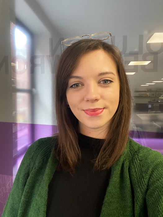 Young white woman, with dark hair, wearing a black t-shirt and green cardigan.