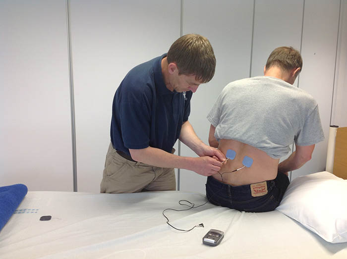 Dr Gareth Jones applying a TENS machine to a patient's lower back as they are sitting down