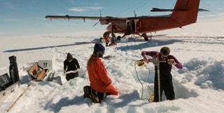 People working in the snow with a plane in the background
