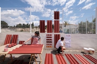 Two artists painting large red roof tiles in an open space
