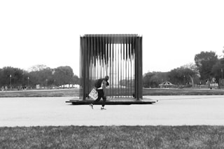 Black man walking past a cage style statue in the centre of an American park carrying a BLM placard