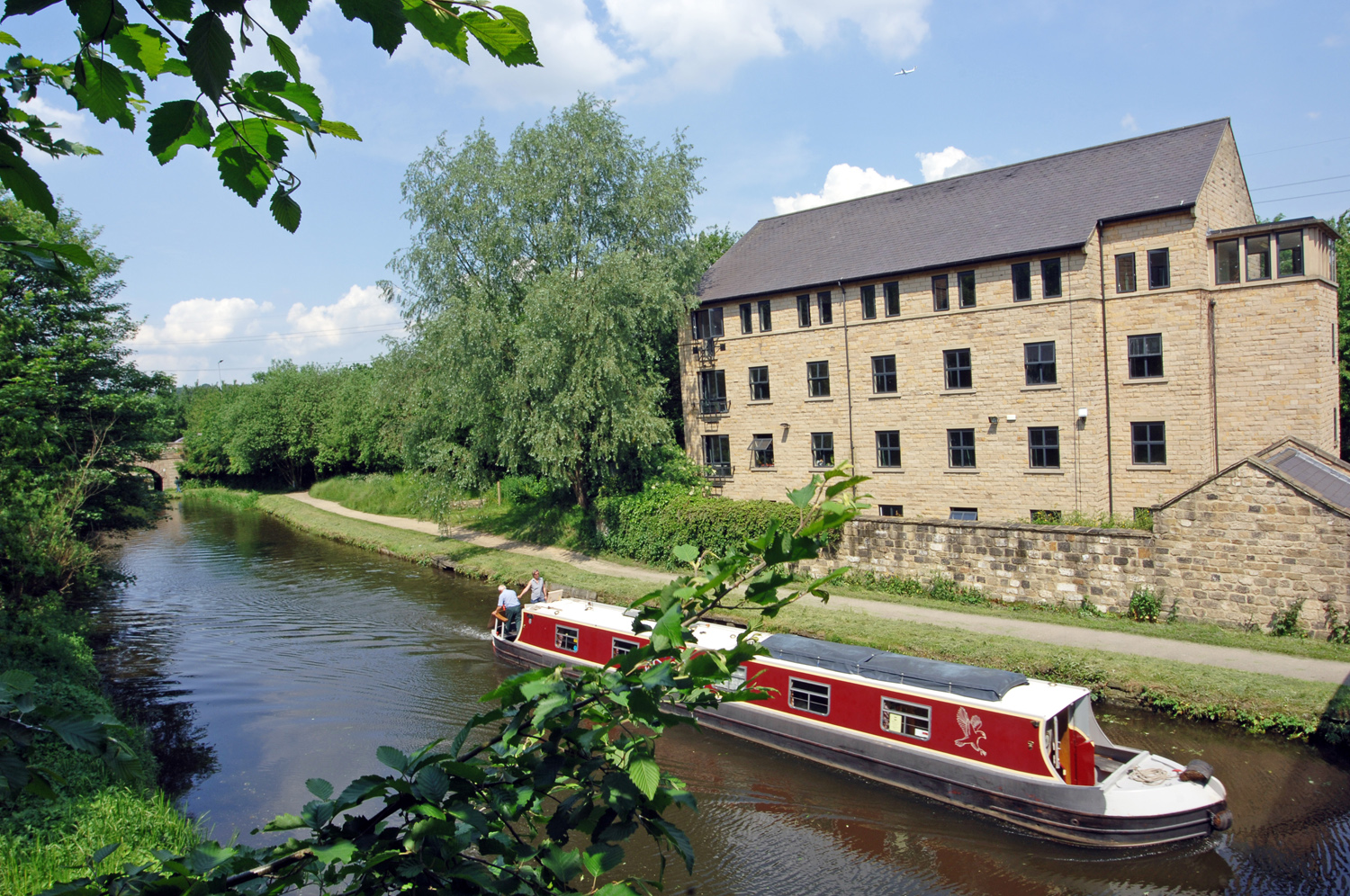 A red and white canal boat travels down the Leeds-Liverpool canal outside Kirkstall Brewery