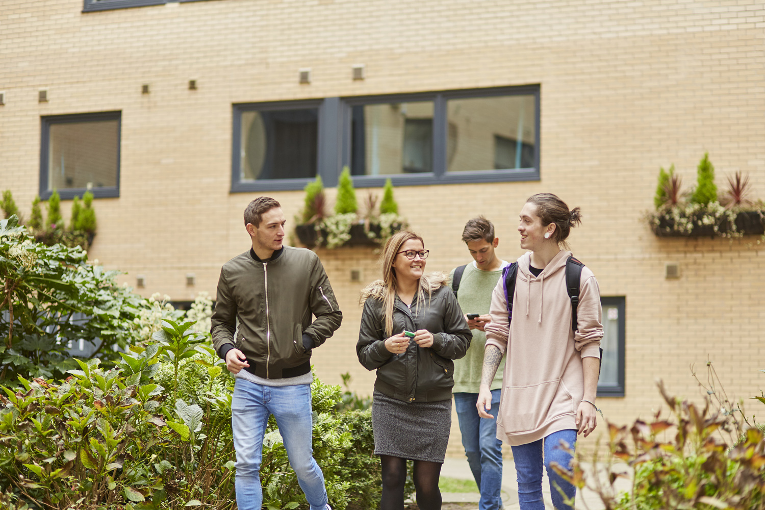 Four students in conversation walking together with Marsden House in the background