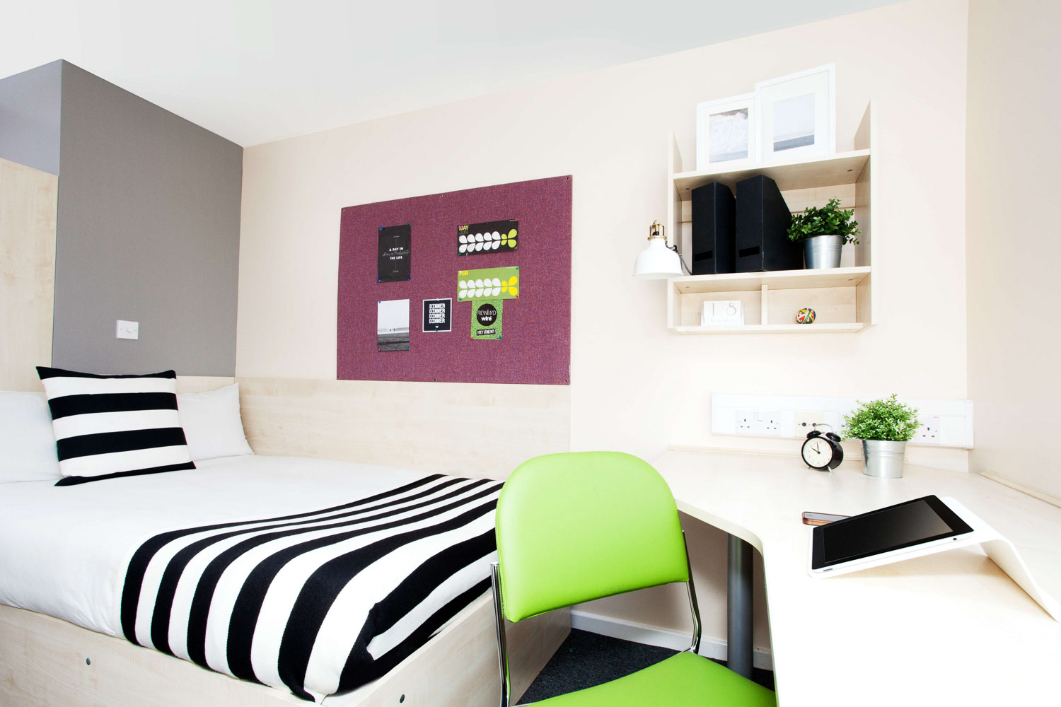 Bedroom with black and white striped bedding a green desk chair and stationery on shelves