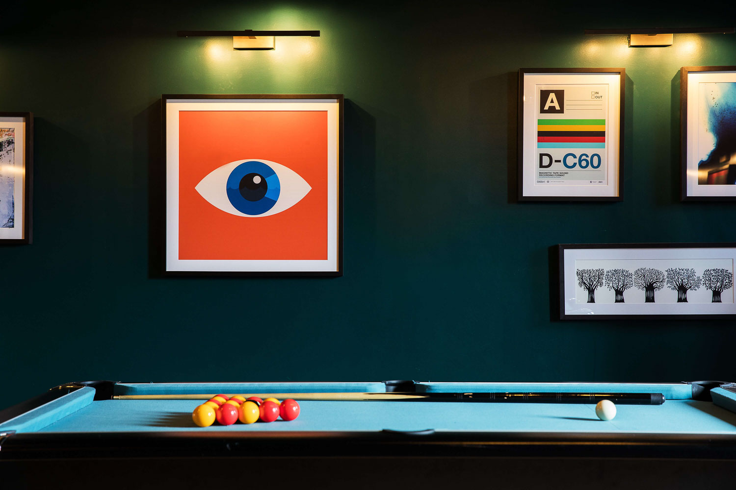 Framed art print of an eye against a dark green wall with a blue snooker table set up in front
