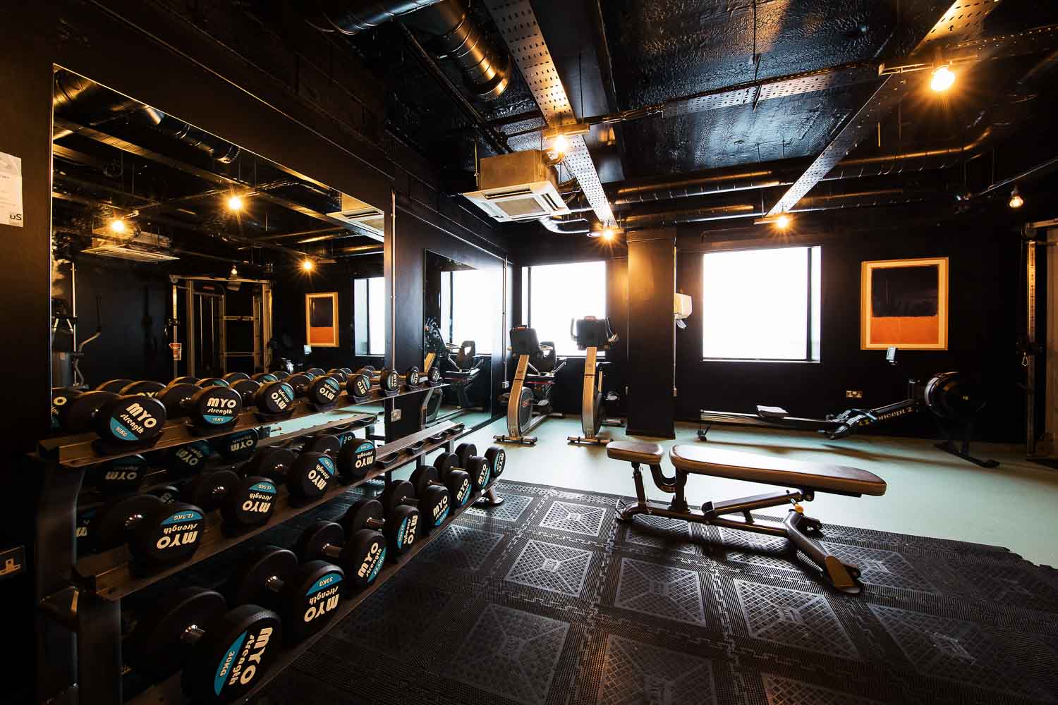 A rack of dumbells and weights equipment exercise bikes against a black wall with windows