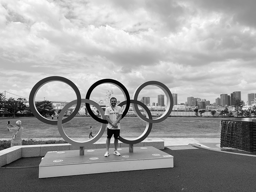 Black and white image of Marc Holdsworth in front of the Olympic rings