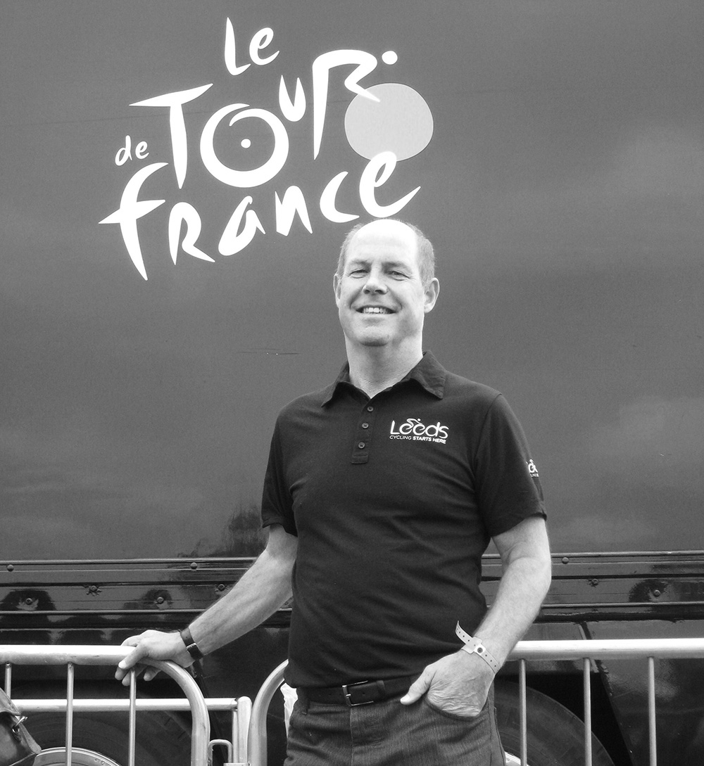 Black and white photograph of Peter Smith in front of the Le Tour De France logo