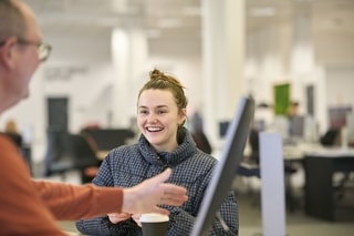 Image of person at Leeds Beckett Library chatting to another person stood by a computer