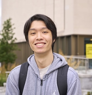 Student from Thailand smiling in a grey hoodie and black backpack