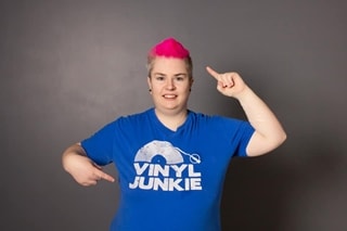 Image of person pointing at their pink hair and slogan on t-shirt