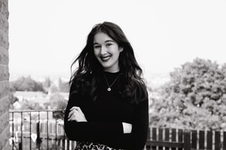 Black and white image of a girl with long brown hair smiling and her arms crossed